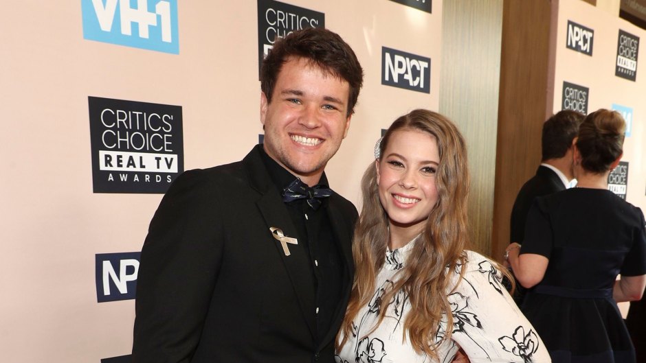 bindi irwin wears a white dress with black print while her fiance chandler powell wore a black shirt, black blazer and khaki pants at the Critics' Choice Real TV Awards 2019 bindi irwin will honor late father steve at wedding