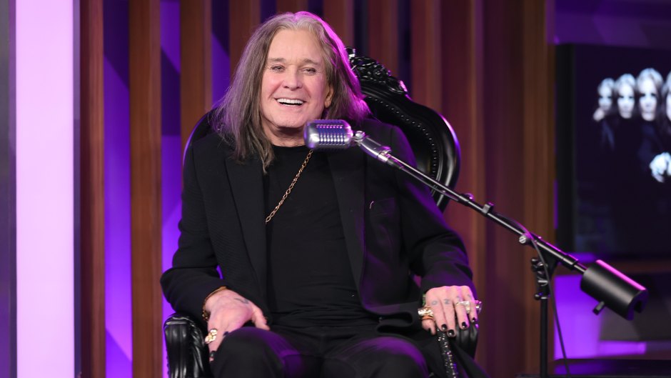 Ozzy Osbourne smiles while sitting in chair in black outfit