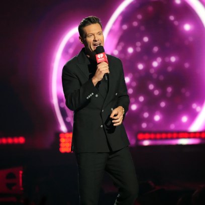 Ryan Seacrest wears black suit while holding microphone