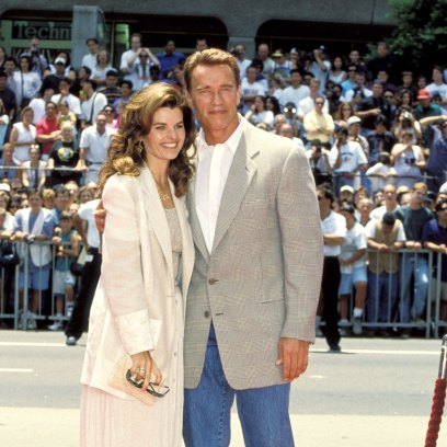 Arnold Schwarzenegger smiles in a suit in front of a crowd with Maria Shriver