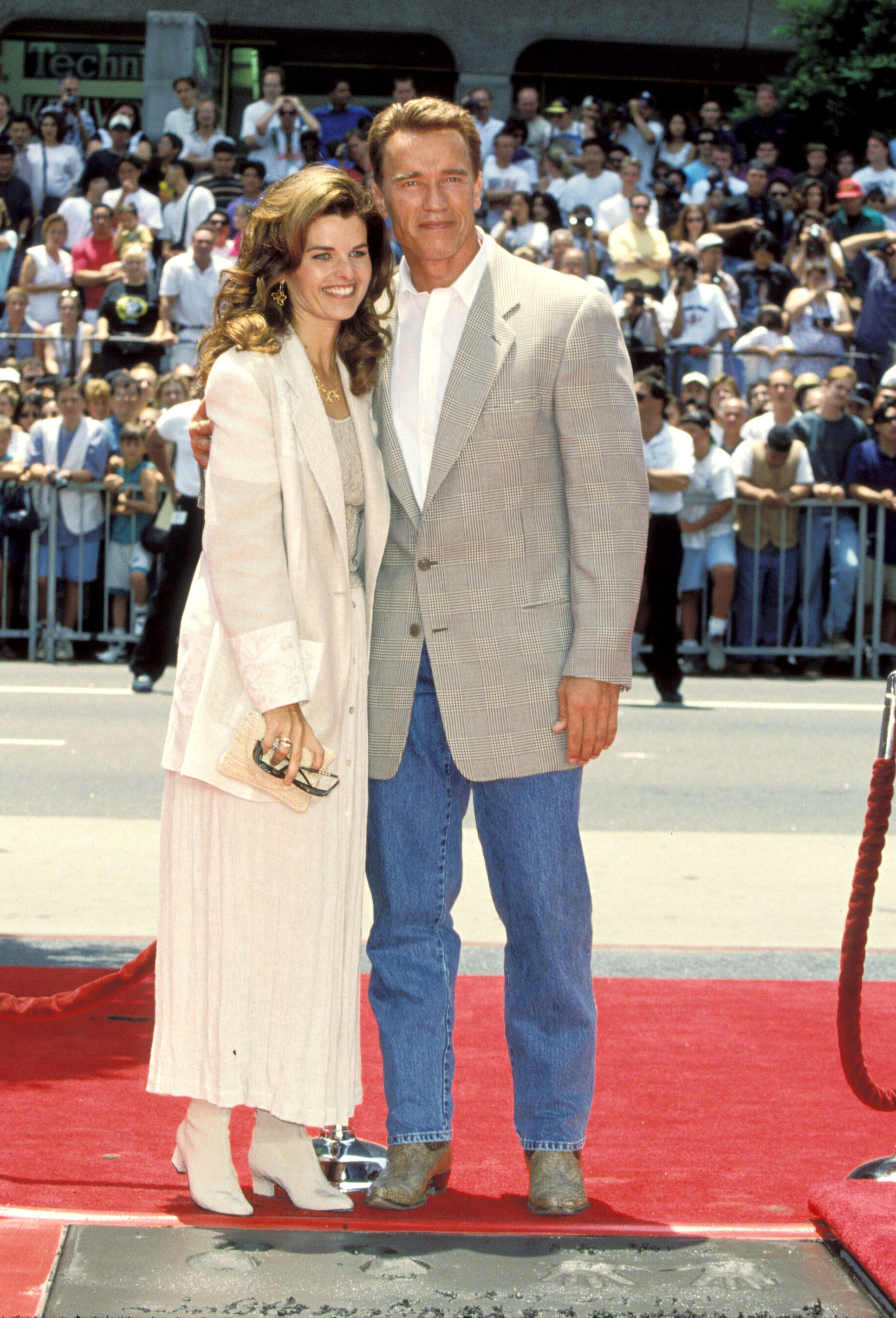 Arnold Schwarzenegger smiles in a suit in front of a crowd with Maria Shriver