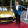 Robert Herjavec smiles while standing next to a gold car