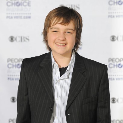 Angus T. Jones smiles while wearing a black suit