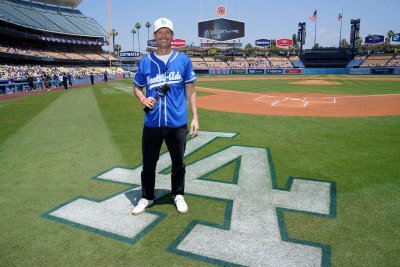 Ryan Seacrest wears baseball jersey and cap while standing on baseball field