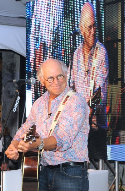Jimmy Buffett performs on stage in patterned shirt and jeans