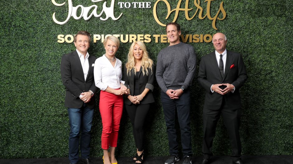 The cast of Shark Tank stands together in front of green backdrop