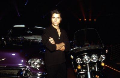 John Stamos wears black outfit while leaning against car