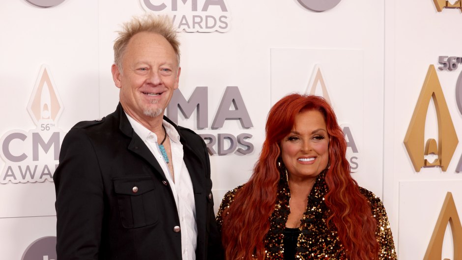 Wynonna Judd wears black dress with gold embellishments next to husband Cactus Moser