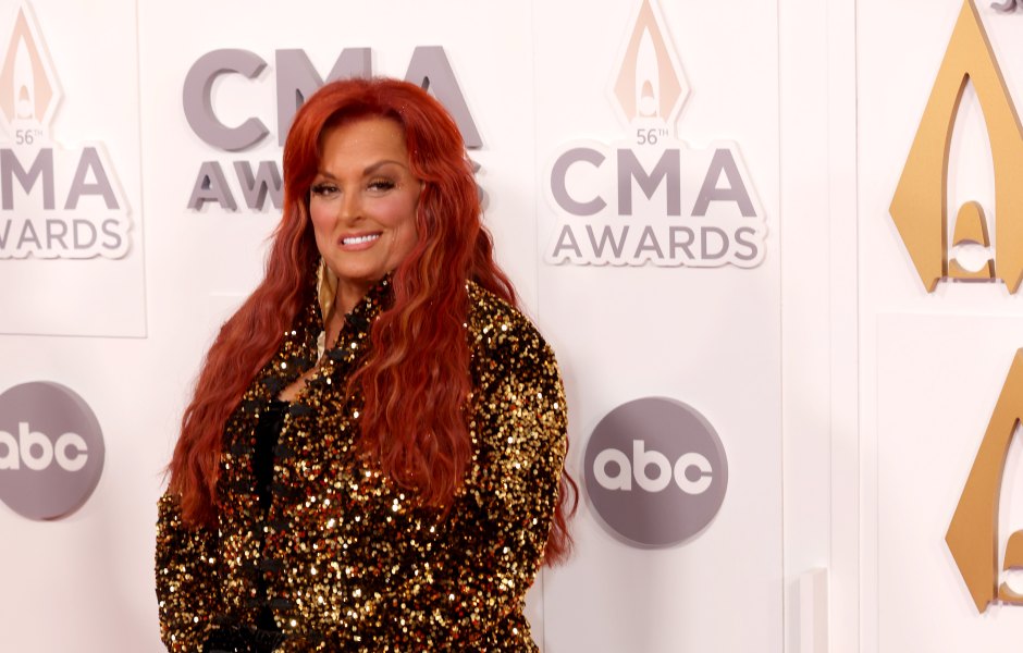 Wynonna Judd smiles while wearing a black dress with gold trim