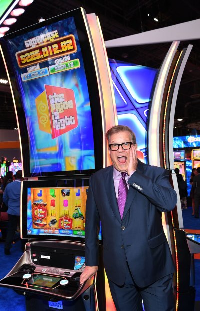 Drew Carey makes surprised face while standing in front of a slot machine