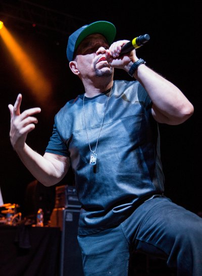 Ice-T performs on stage in a leather shirt and black pants with a baseball cap