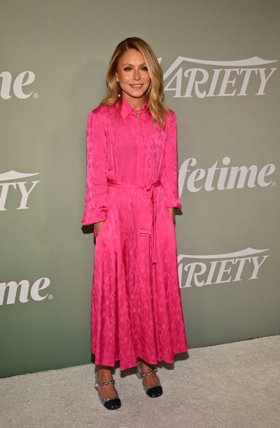 Kelly Ripa stands with hands in pockets while wearing pink dress