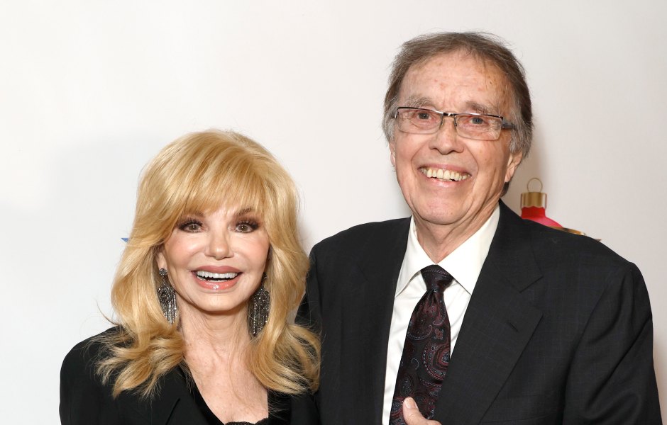 Loni Anderson smiles while wearing a black blazer and skirt next to husband Bob Flick