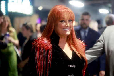 Wynonna Judd smiles in a black jacket with red details