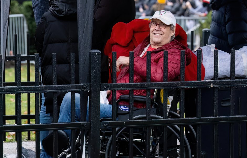 Chevy Chase wears red jacket and baseball cap while sitting in wheelchair