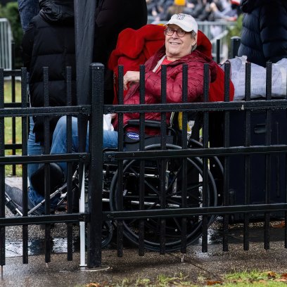 Chevy Chase wears red jacket and baseball cap while sitting in wheelchair