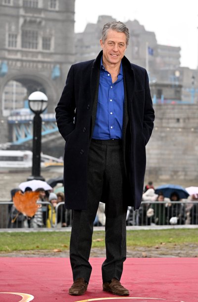 Hugh Grant in black coat and slacks with a blue shirt