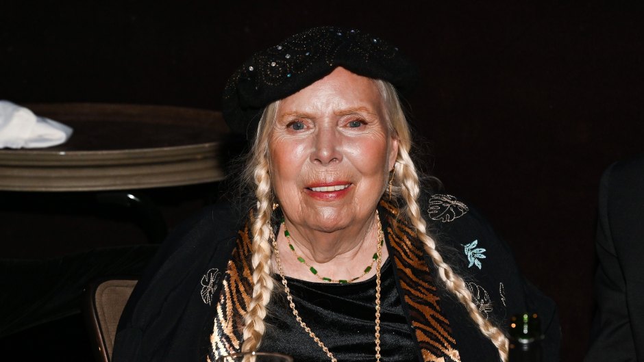Joni Mitchell wears her hair in braided pigtails with a black top.