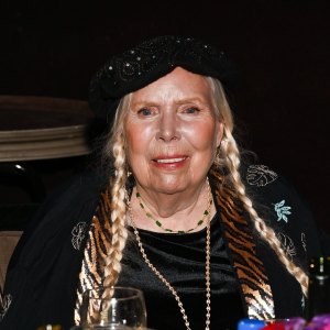Joni Mitchell wears her hair in braided pigtails with a black top.